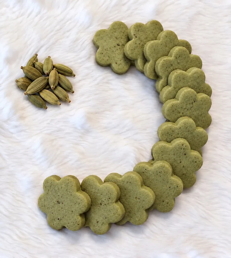 Flower-shaped cardamom butter cookies with cardamom pods on a white fuzzy surface
